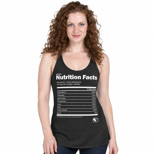 A woman with curly red hair wearing a dark heather gray racerback tank top with a white 'Nutrition Facts' graphic printed on the front, set against a plain white background.