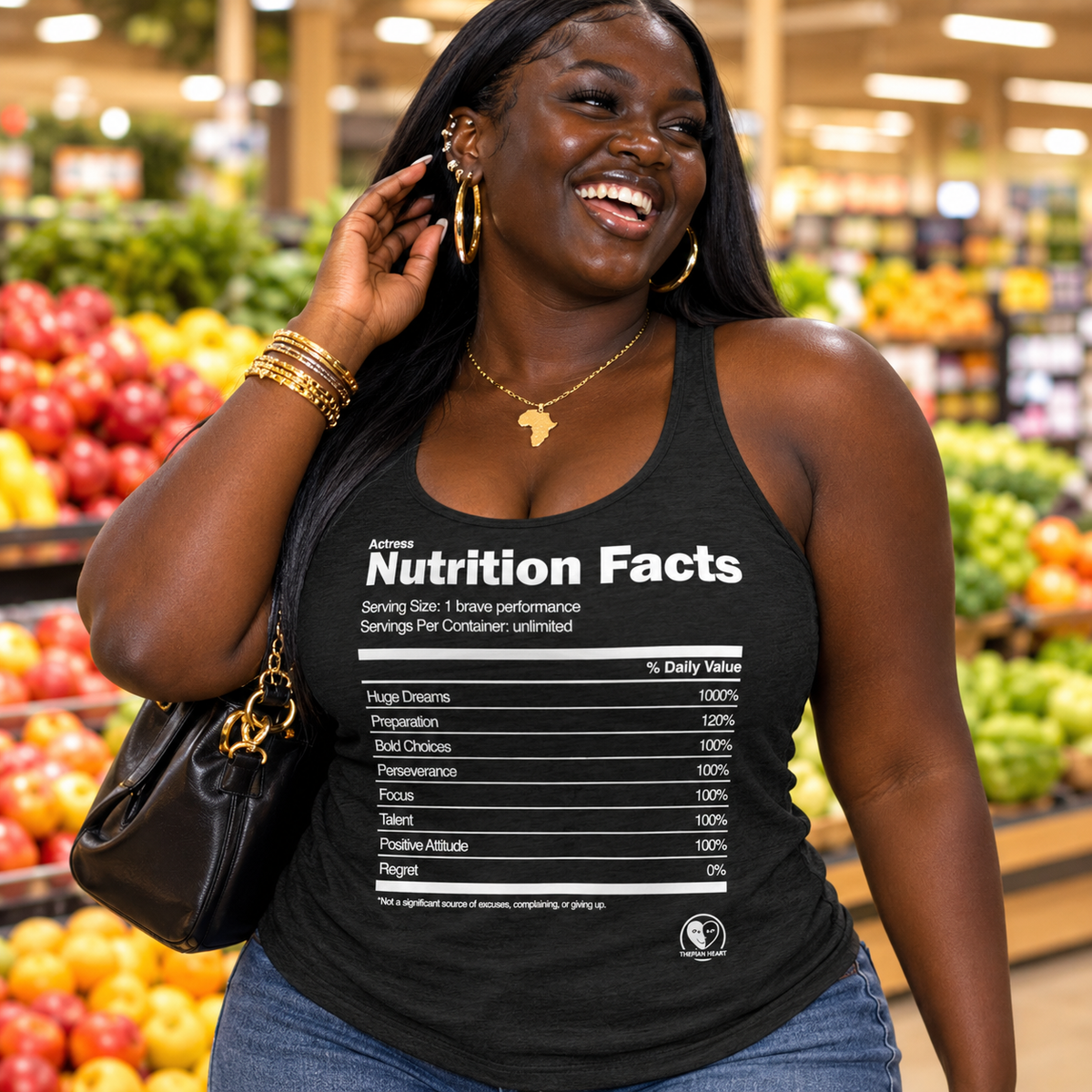 A woman in a grocery store wearing a black graphic tank top with a white 'Nutrition Facts' table print, blue jeans, gold jewelry, and a black handbag.