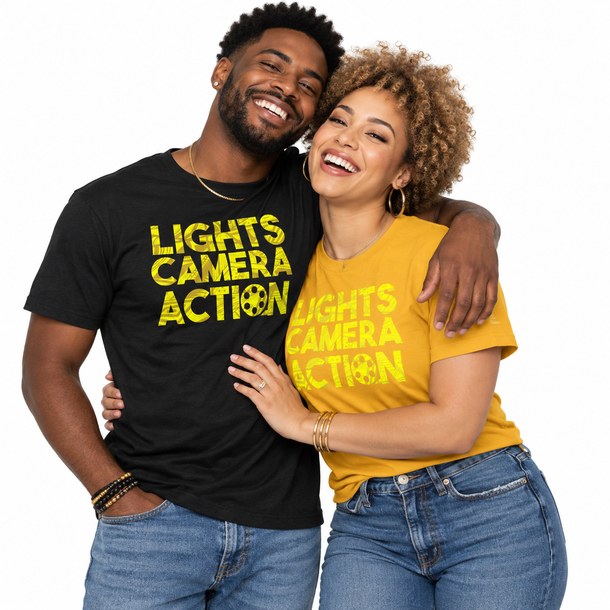 A man and a woman hugging and smiling while wearing matching graphic t-shirts. The man wears a black t-shirt with yellow text reading 'LIGHTS CAMERA ACTION' and a peace sign, and the woman wears a yellow t-shirt with the same text.