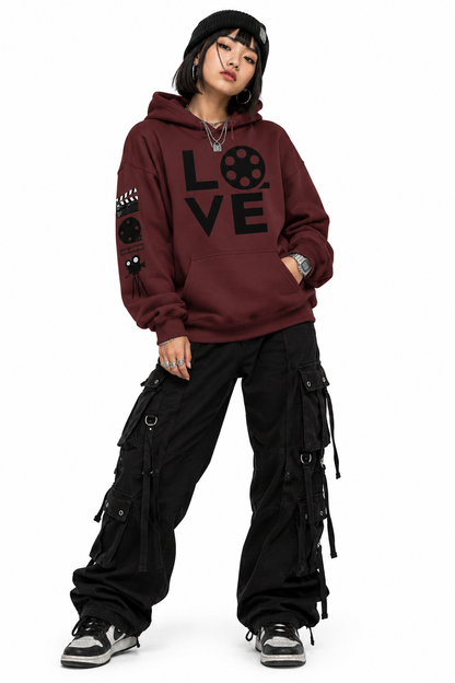 A woman with black hair wearing a maroon fleece hoodie with a black graphic print that spells 'LOVE' using a film reel and clapperboard. She is stylish and cool.
