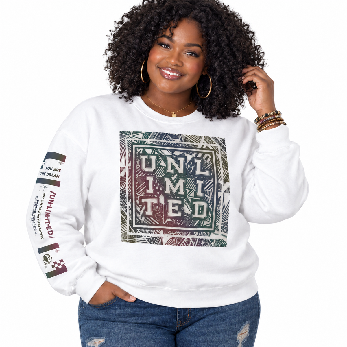 A woman with curly black hair wearing a white crewneck sweatshirt with a large graphic print on the front and text on the sleeve, paired with blue jeans, against a plain white background.