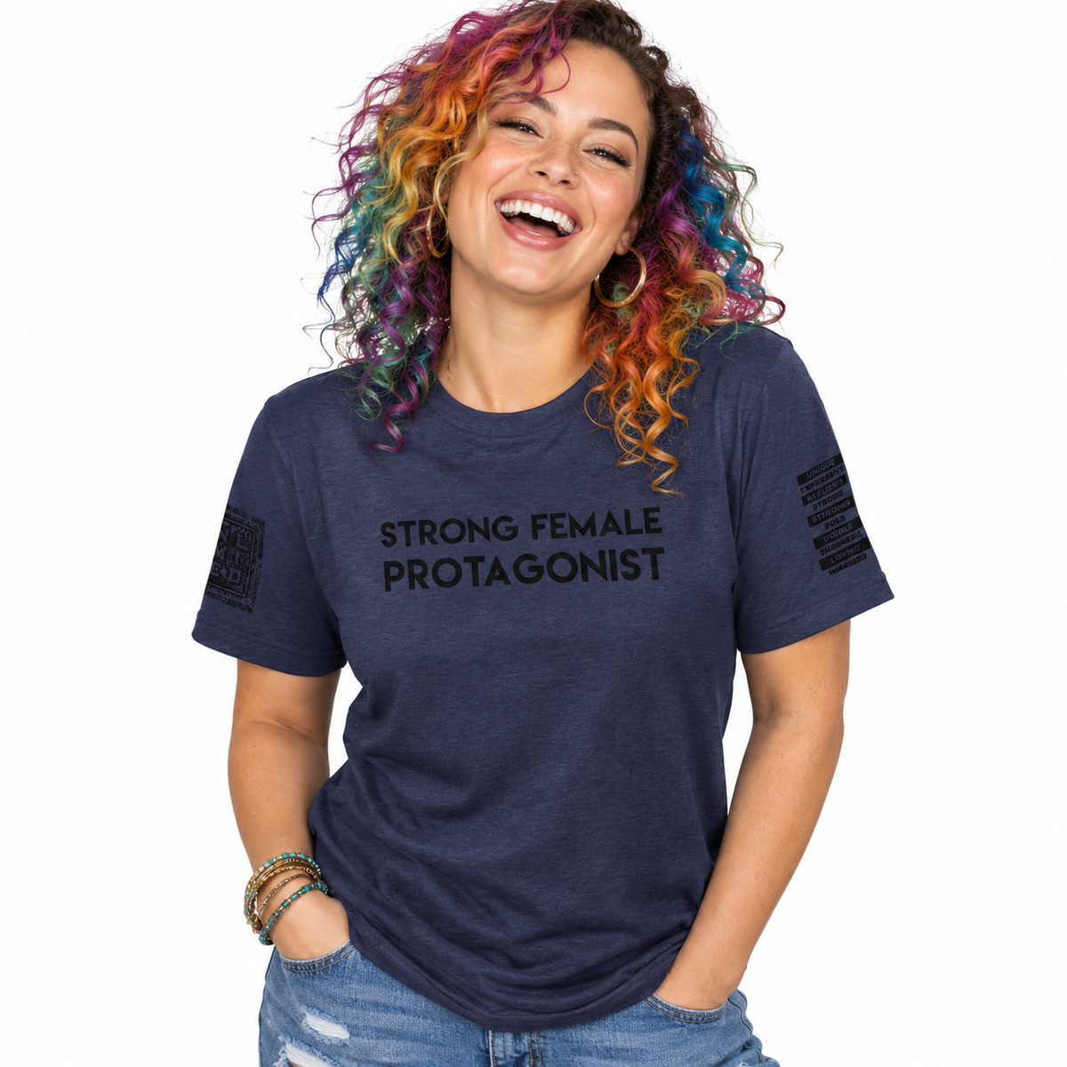 A woman with vibrant rainbow-colored curly hair is smiling and laughing while wearing a heather navy blue t-shirt with the text 'STRONG FEMALE PROTAGONIST' printed in black across the chest. She is also wearing blue jeans and bracelets, set against a plain white background.