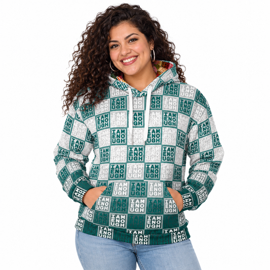 A woman wearing a green and white patterned hoodie with the text 'I AM ENOUGH' repeated across the fabric, paired with light blue jeans, against a plain white background.