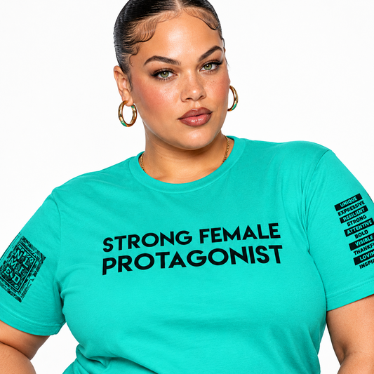 A woman wearing a bright turquoise short-sleeve graphic T-shirt with the words 'STRONG FEMALE PROTAGONIST' printed in black across the chest, plus black text graphics on both sleeves, against a plain white background.
