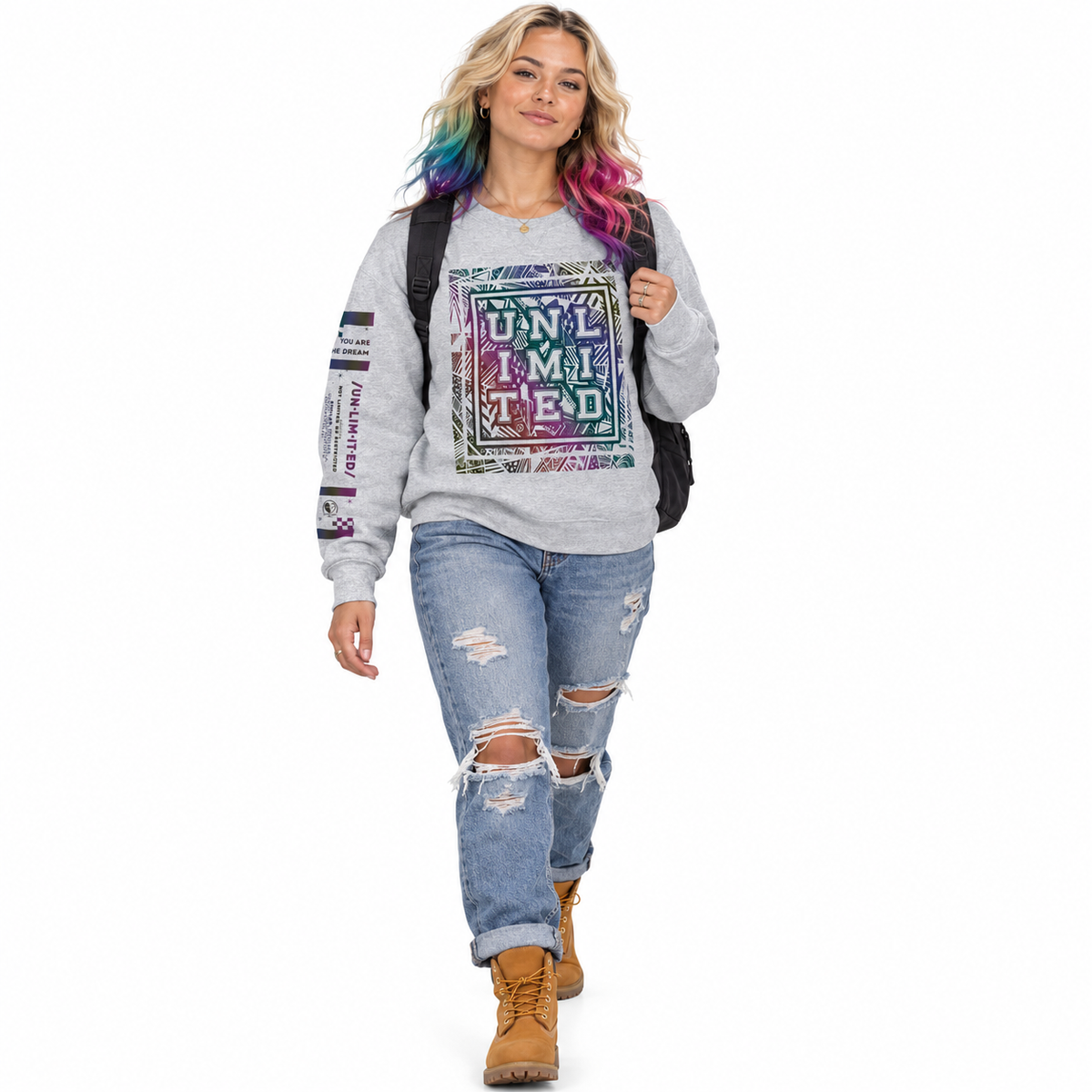 A woman modeling a light gray crewneck sweatshirt with a colorful graphic print that reads 'UNLIMITED' and 'UNLIMITED' on the front, paired with distressed blue jeans and brown boots, against a plain white background.
