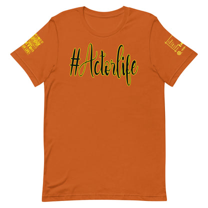 An orange short-sleeve crewneck t-shirt featuring the text '#Actorlife' printed across the chest in black script with a yellow outline. The left sleeve has a yellow graphic with the words 'Tired of being a nobody', and the right sleeve features a small yellow graphic with a microphone and the word 'KING'.